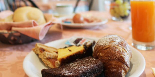 Colazione con dolci, croissant e succo d'arancia su tavola imbandita.