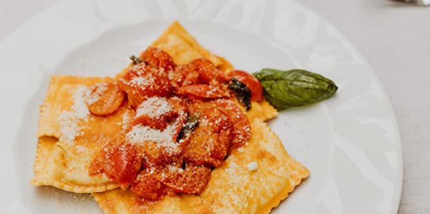 Ravioli con salsa di pomodoro, basilico e formaggio grattugiato su piatto bianco.